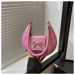 Close-up of pink crescent handbag with textured finish and gold bow buckle detail