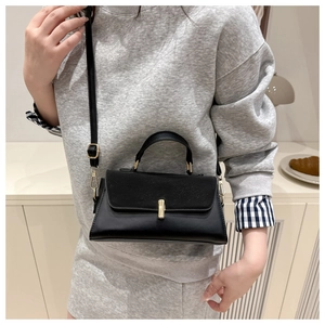 Detail of black leather crossbody bag with golden cylindrical twist lock on model