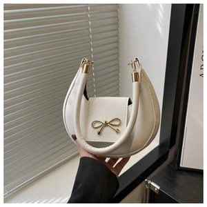 Detail of white Saffiano leather texture and golden bow clasp on a handbag