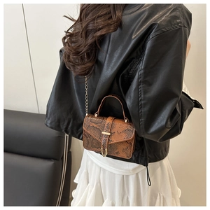 Detail of a brown snakeskin mini square bag with golden chain strap on a fashion model