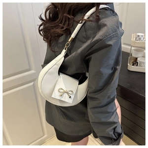 Side view of white crescent shoulder bag with golden bow decoration on female model
