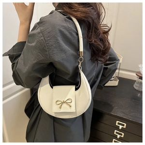 Close-up of a white crescent shoulder bag with golden bow and cross-grain leather texture