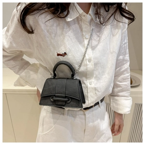 Detail view of mini black hourglass bag with curved handle and metal chain on a model