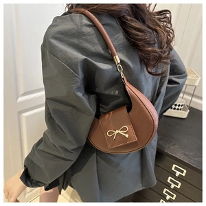 Close-up of brown crescent bag with golden bow hardware and cylindrical shoulder strap