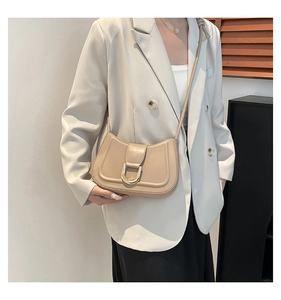 Dettaglio della borsa in pelle opaca albicocca con fibbia a D dorata su blazer bianco