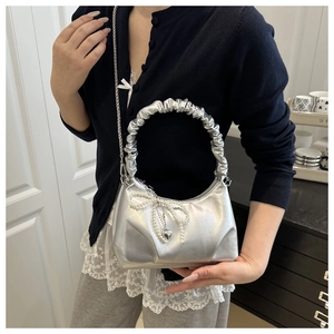 Silver metallic bag with pearl bow and heart charm worn as a stylish crossbody bag