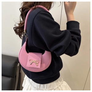Pink crescent underarm bag with grainy leather texture and gold bow detail on model