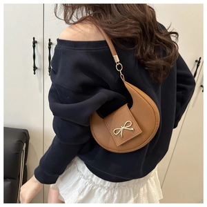 Detail of caramel crescent shoulder bag with golden bow clasp and sleek leather finish