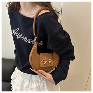 Detail of a brown crescent bag with荔枝 grain leather and a golden bow buckle