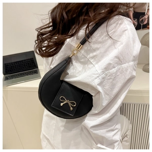 Detail of a black crescent shoulder bag with a gold bow buckle on the flap
