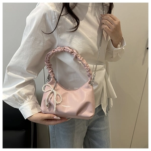 Detailed shot of pink pleated shoulder bag with pearl bow charm and silver chain strap