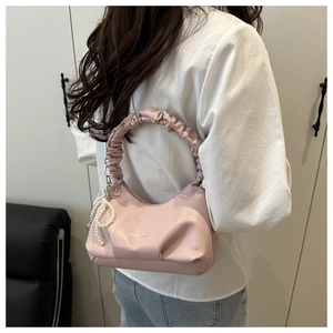 Pink pleated underarm bag with pearl bow charm and shoulder strap shown on a model