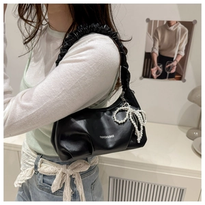 Detail of black crescent shoulder bag with pleated handle and pearl bow charm accessory