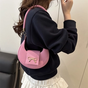 Pink crescent underarm bag for women with golden bow buckle on a textured leather surface
