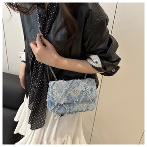 Détail du sac bandoulière en jean bleu clair avec bords effilochés et chaîne argentée