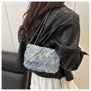 Détail d'un sac bandoulière en denim bleu clair avec matelassage effiloché et chaîne