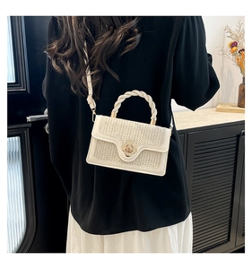 Detail of woven cream crossbody bag with gold floral clasp and twisted top handle
