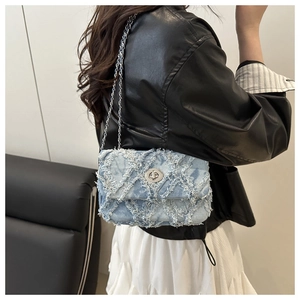 Détail d'un sac bandoulière en denim bleu clair avec matelassage et bords effilochés