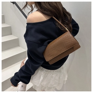 Detail of dark brown woven texture baguette bag with flap closure and braided shoulder strap