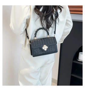 Detail of black woven bag featuring a gold floral clasp and twisted top handle