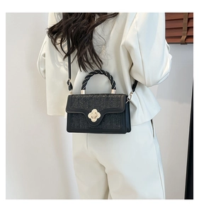 Detail of a black woven crossbody bag with gold floral lock and twisted handle shown on model