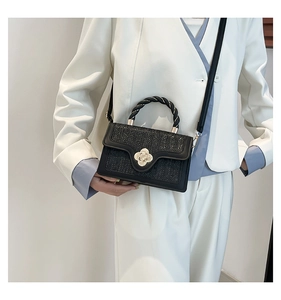 Detail of black woven texture handbag with golden flower clasp on a fashion model