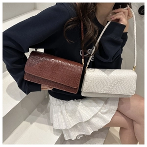 Detail of white and dark brown croc-effect shoulder bags held by a model on steps