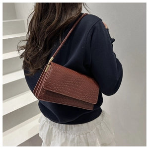 Close-up of retro reddish-brown crossbody bag with embossed crocodile pattern texture