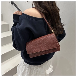 Brown crocodile pattern shoulder bag shown on model with blue top on white stairs