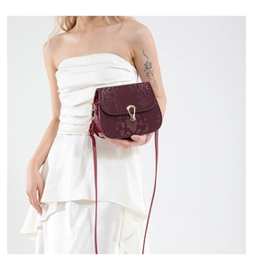 Detail of burgundy snakeskin patterned saddle bag featuring a gold waterdrop buckle lock
