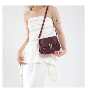 Detail of burgundy snakeskin texture saddle bag with golden metal clasp on white dress