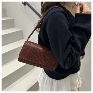 Detail of a dark red woven texture underarm bag held by a model on white stairs