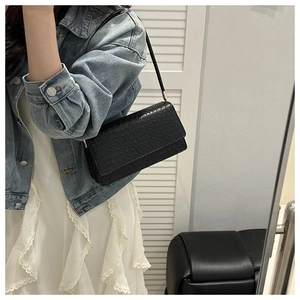 Detail of black faux crocodile texture underarm bag worn by model with casual denim