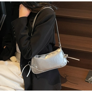 Macro shot of silver metallic shoulder bag with side bow detail and smooth surface texture