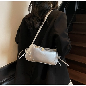 Detail of silver metallic underarm bag featuring side bow ties and stud accents