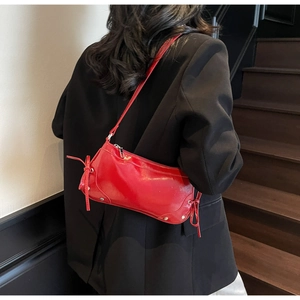 Detail of red glossy shoulder bag with bow accents and silver studs on black blazer