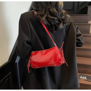 Close-up of red patent leather shoulder bag with bow knot and silver rivet details