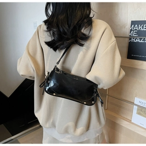 Detail of black glossy leather shoulder bag with silver studs and side ribbon accents