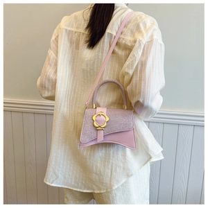 Détail du sac bandoulière rose avec boucle fleur dorée porté par un mannequin en blanc