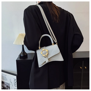 Détail du sac à main argenté texturé avec boucle fleur dorée et rabat asymétrique