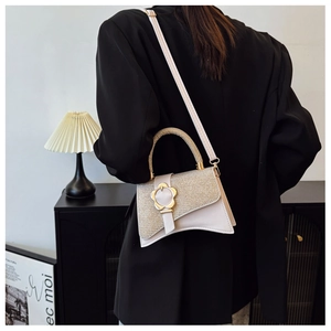 Détail du sac crème avec rabat à paillettes argentées et boucle fleur dorée élégante