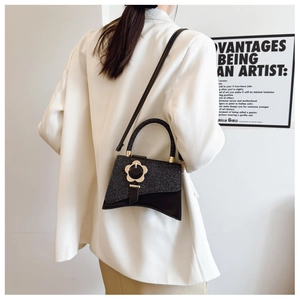 Détail du sac à bandoulière à paillettes noires avec boucle florale dorée sur veste