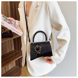Mini borsa a tracolla glitterata nera con fibbia a fiore dorata indossata su blazer bianco