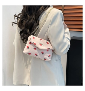 Pink corduroy crossbody bag with red strawberry patterns and gold chain strap detail