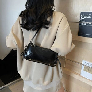 Retro black glossy leather underarm bag with silver studs worn by a model in a cozy setting