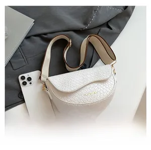 Detailed shot of white saddle bag with woven texture and wide canvas strap on office desk
