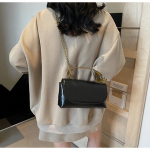 Detail of black glossy crossbody bag with gold circular handle and chain strap on model