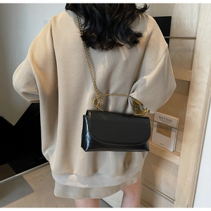 Detail of black crossbody bag with gold half-circle handle and metal chain strap on model