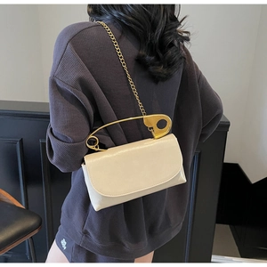 Detail of cream crossbody bag featuring a large gold safety pin handle and chain strap