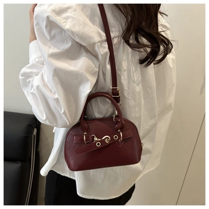 Deep red textured shell bag with golden metal ring and buckle detail on a model